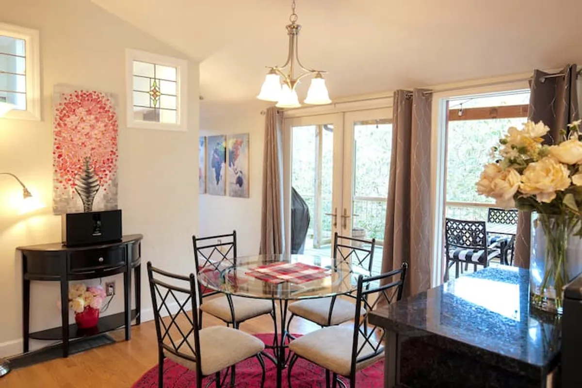 A bright and cheerful dining area centered around a glass table, adorned with a vibrant floral arrangement and colorful artwork on the walls. The setting is designed for intimate family meals or celebratory dinners, with a welcoming ambiance that encourages conversation and connection.