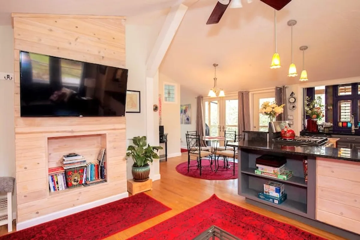 This interior image offers a wide view that includes a television, a rustic wooden accent wall, the dining area, a kitchen island, and a stylish area rug. It portrays a welcoming environment where family gatherings, shared meals, and entertaining are central activities.