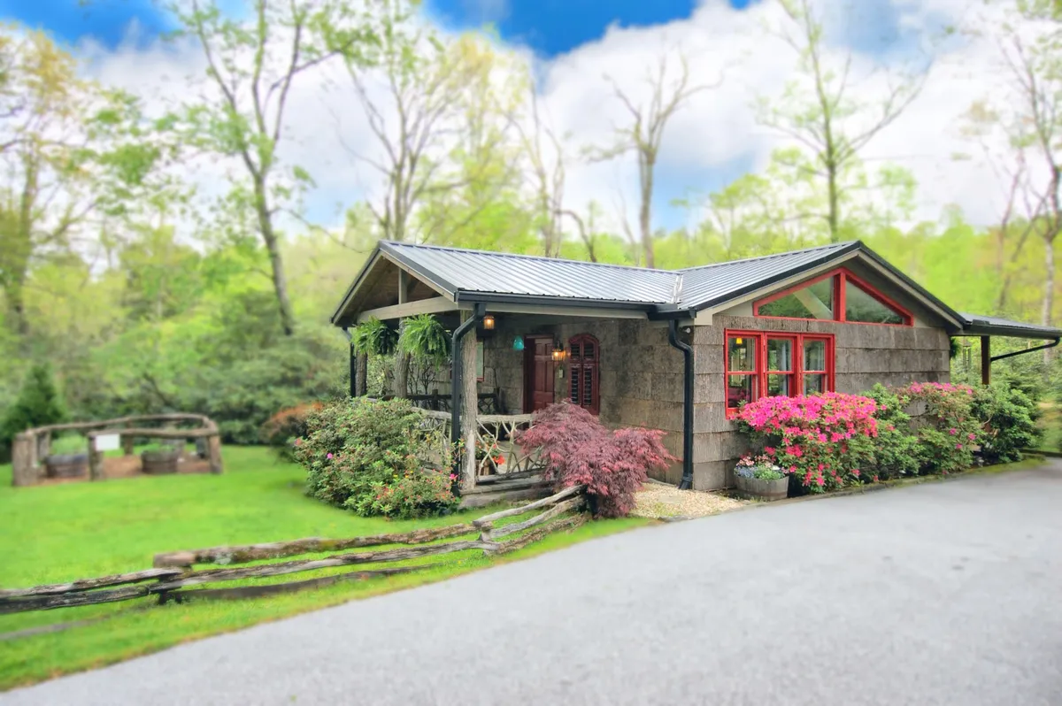 A view of the cozy cabin set against vibrant flower beds and a rustic wooden railing. The scene gives a sense of tranquility, with the garden in bloom and the porch offering a comfortable place to relax, enjoy morning coffee, or simply soak in the mountain air.