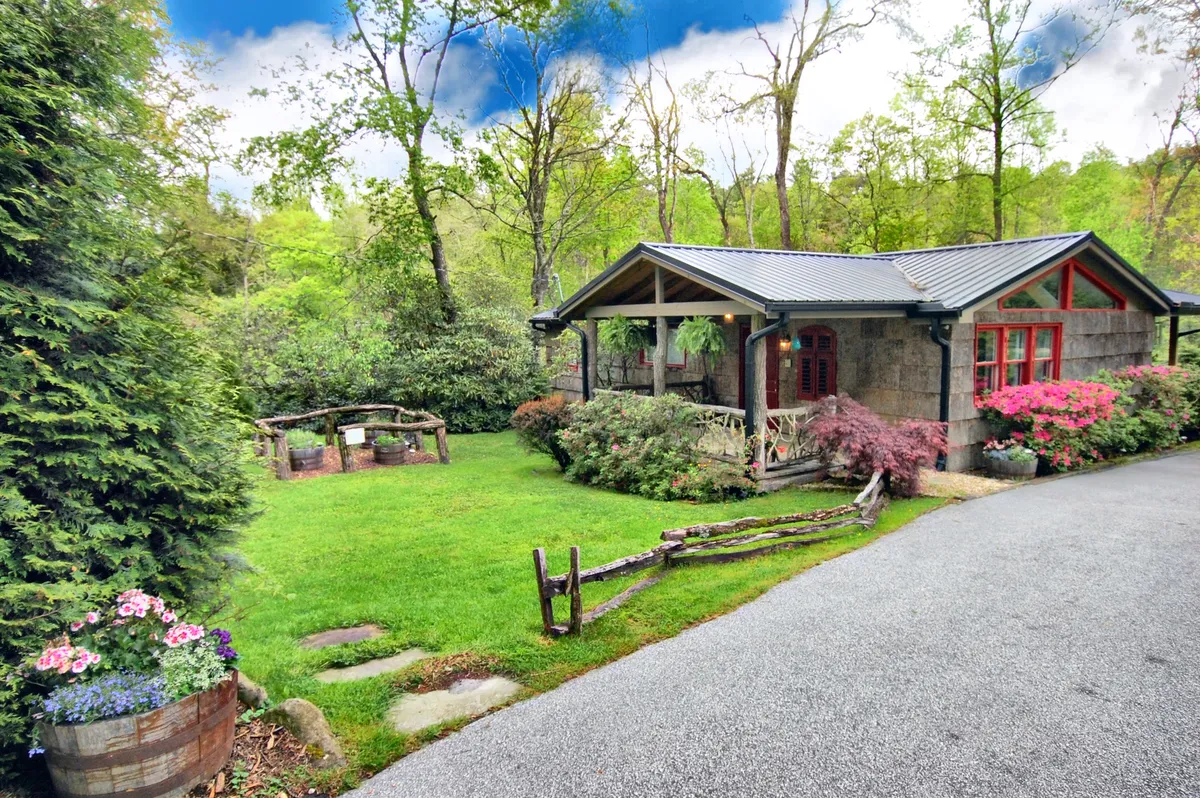 The image features a charming single-family cottage surrounded by a lush, vibrant garden, colorful flower pots lining the entry, and a classic wooden fence. The porch offers inviting sunset views, creating an atmosphere perfect for morning coffee or relaxing evenings outdoors. The scene radiates tranquility and warmth, with touches of nature and comfort visible throughout.
