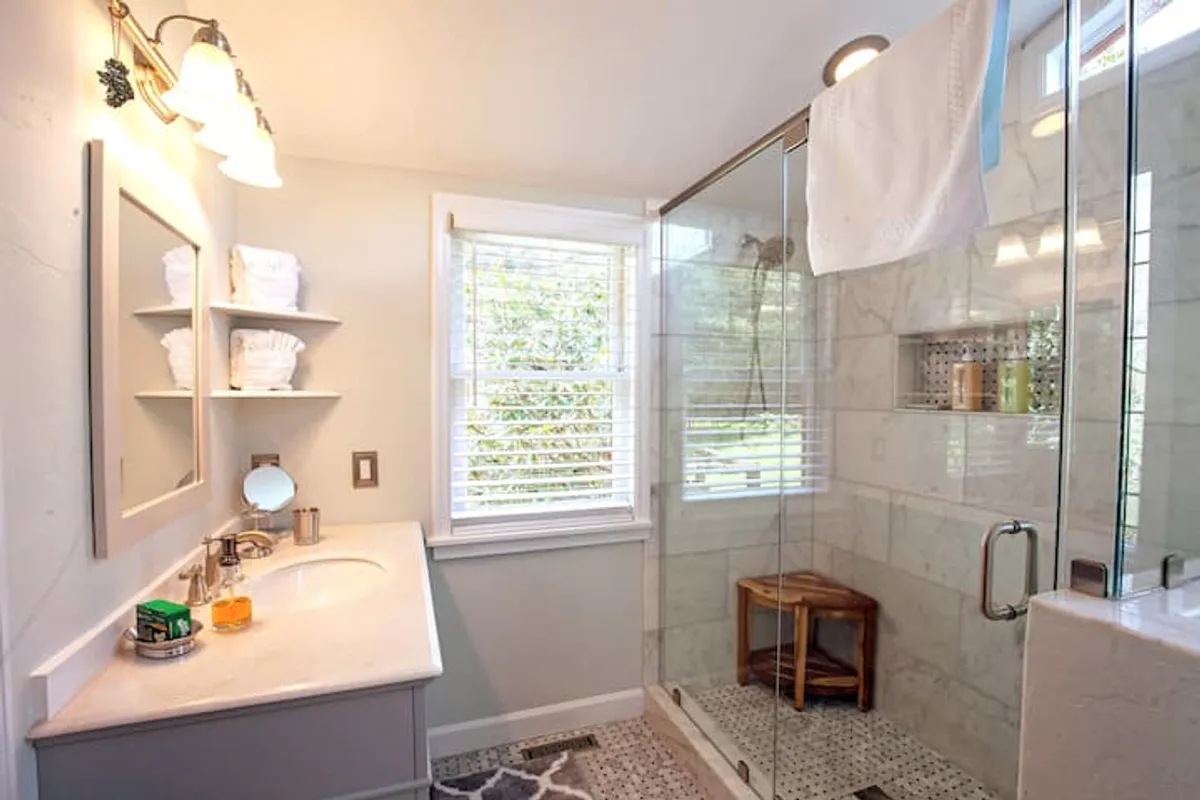 A serene en-suite bathroom features a glass shower enclosure, a vanity with mirror, and a window letting in natural light. The calm design evokes a sense of rejuvenation and relaxation, ideal for unwinding after a day of adventure.